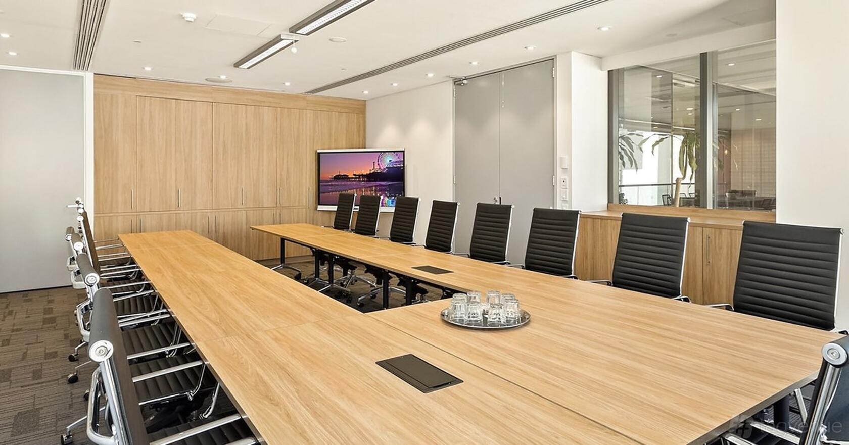 A coworking meeting room with a U-shaped wooden table, black chairs, and wall-mounted screen at Workspace365 66 Clarence St.