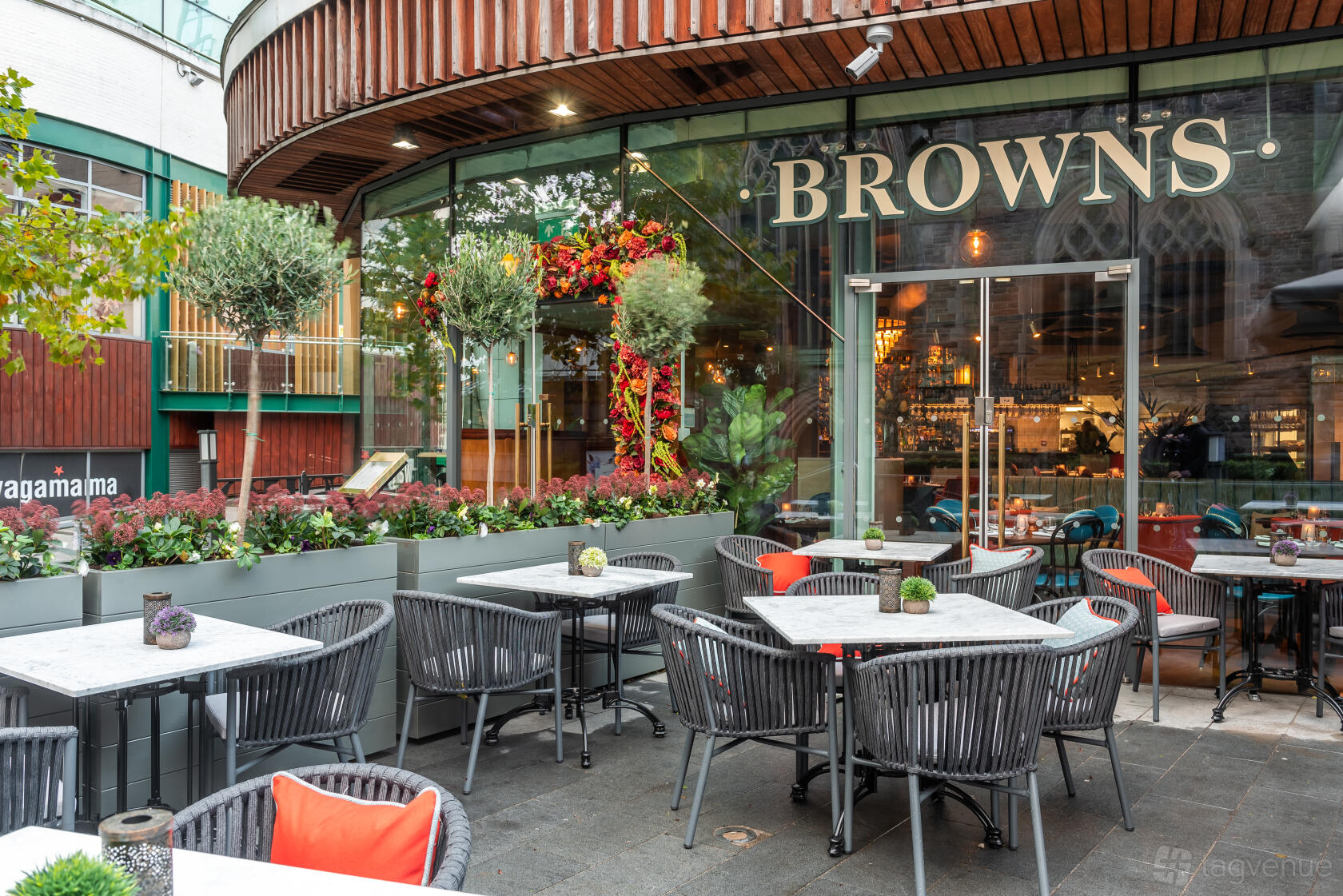 A restaurant with outdoor seating, marble-top tables, and greenery in front of Browns Brasserie & Bar Birmingham.