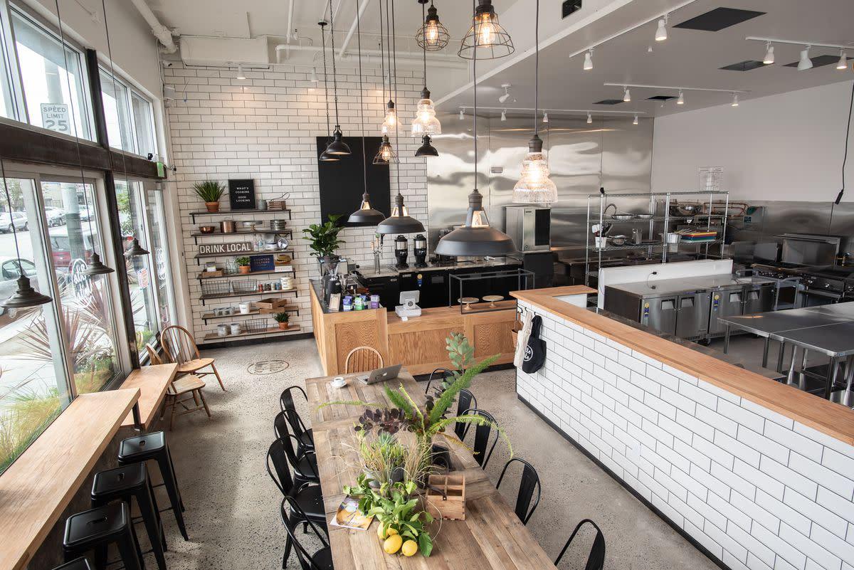 An open kitchen with white subway tile walls, industrial lighting, and a large wooden table at Prime Kitchen & Event Space BiteUnite.