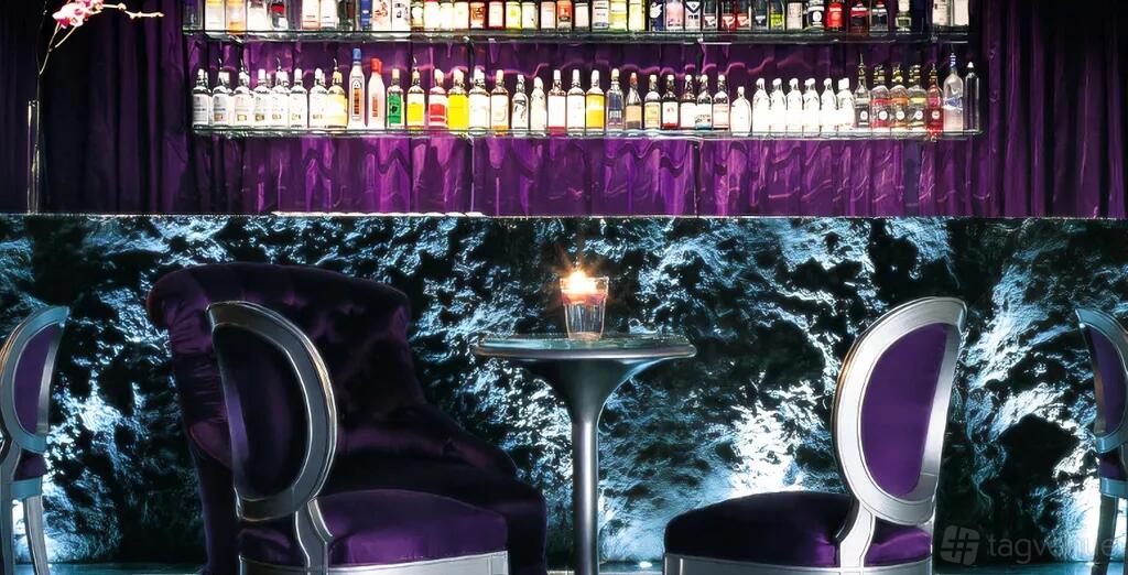 A hotel bar with purple velvet chairs, a candlelit table, and a mirrored back bar stocked with spirits at Sanderson London.