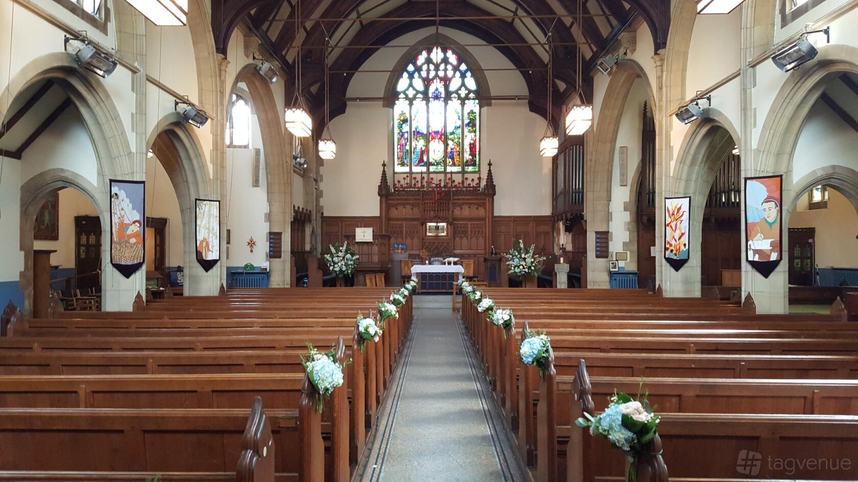 A church sanctuary with wooden pews, stained glass windows, and floral aisle decorations at St Paul's UR Church and halls Croydon.