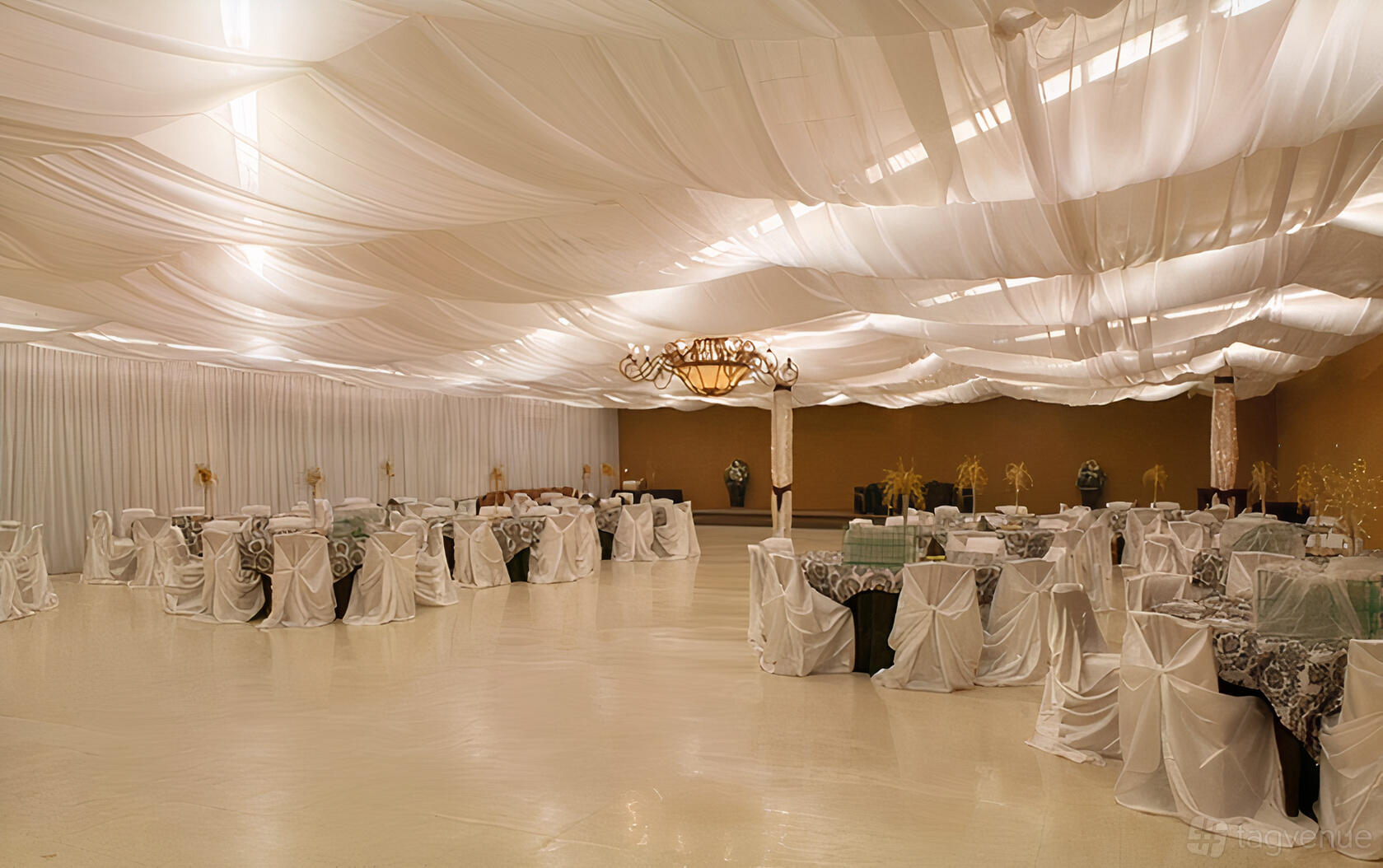 An event venue with draped white ceilings, chandeliers, and round tables covered in white linens at JS Venue Plus.