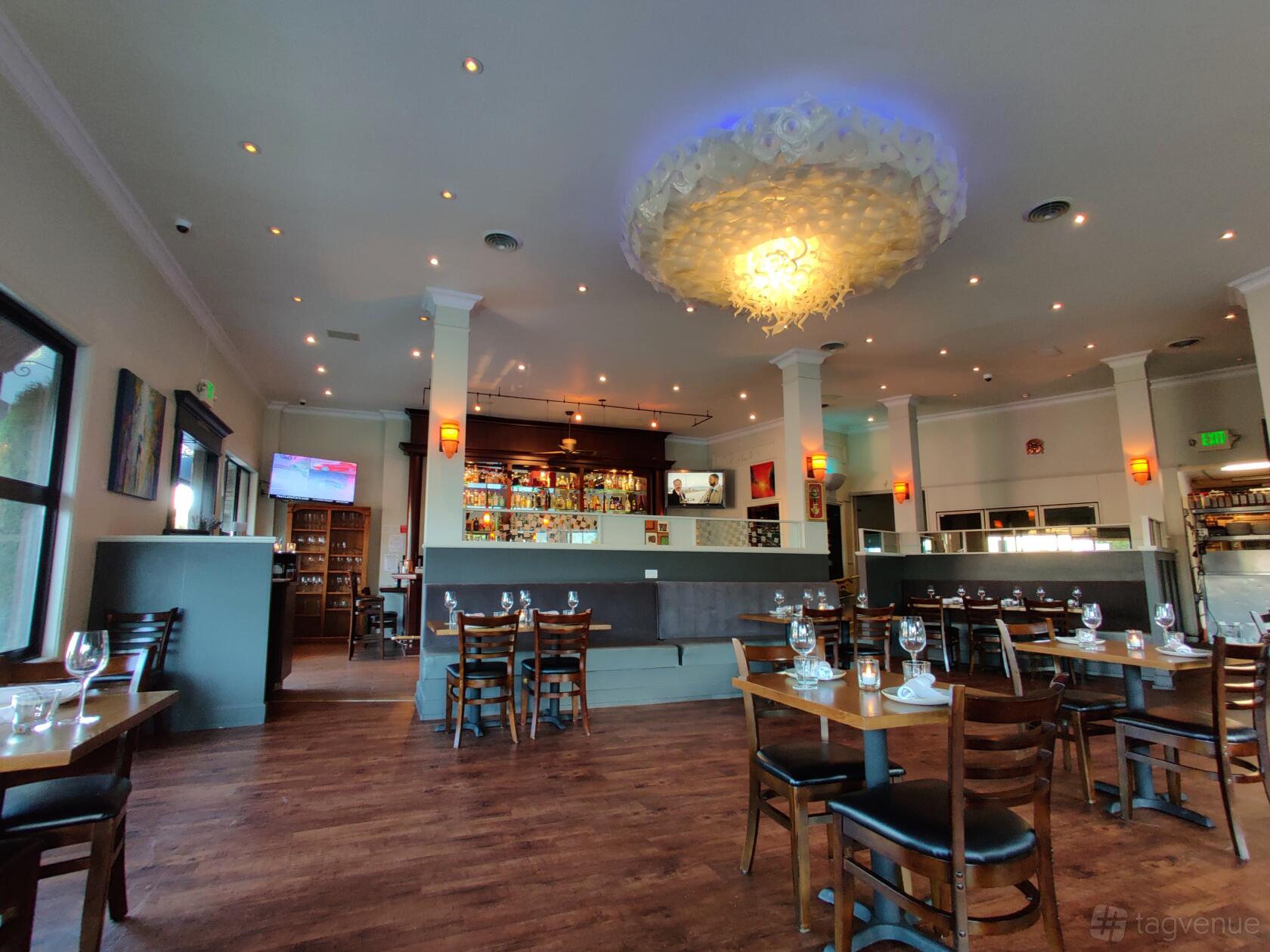 A restaurant with wooden floors, set dining tables, a decorative ceiling light, and a bar area at Aji Limo Peruvian.