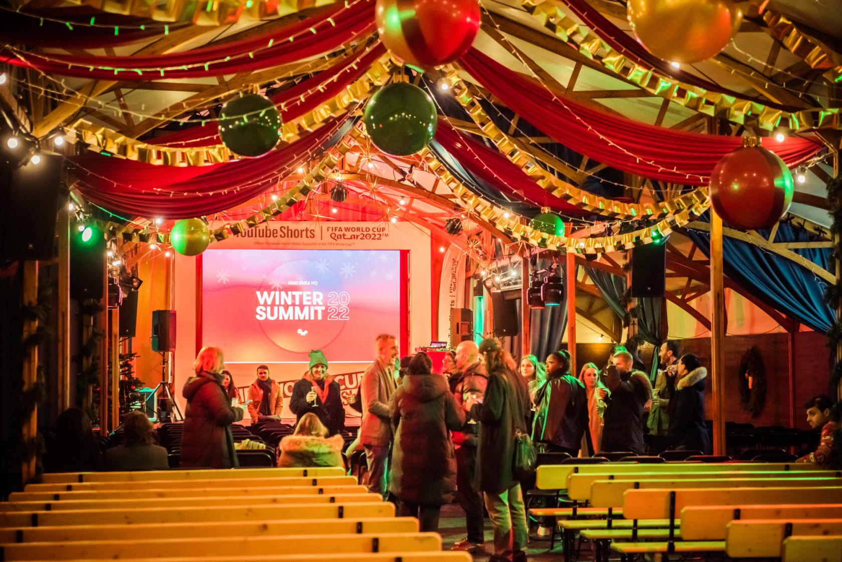 An event venue with wooden benches, festive draped fabric, and hanging ornaments at Between the Bridges.
