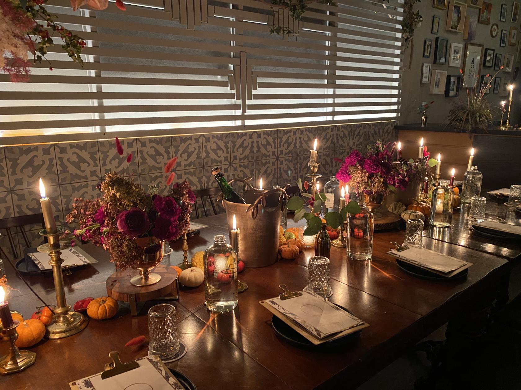 An event space in a restaurant with a long wooden table set with candles, fresh flowers, pumpkins, and glassware at Festival Cafe NYC.
