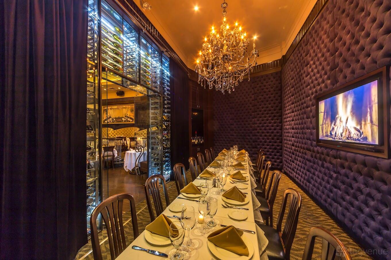 A dining room with a long table set with gold napkins, chandelier lighting, and a fireplace at Empire Steak House East.