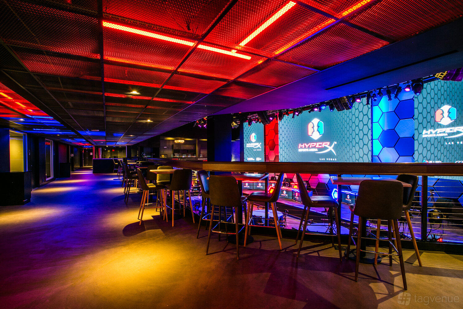 An event space with colorful LED lighting, high-top tables, and a view of large digital screens at HyperX Arena Las Vegas.