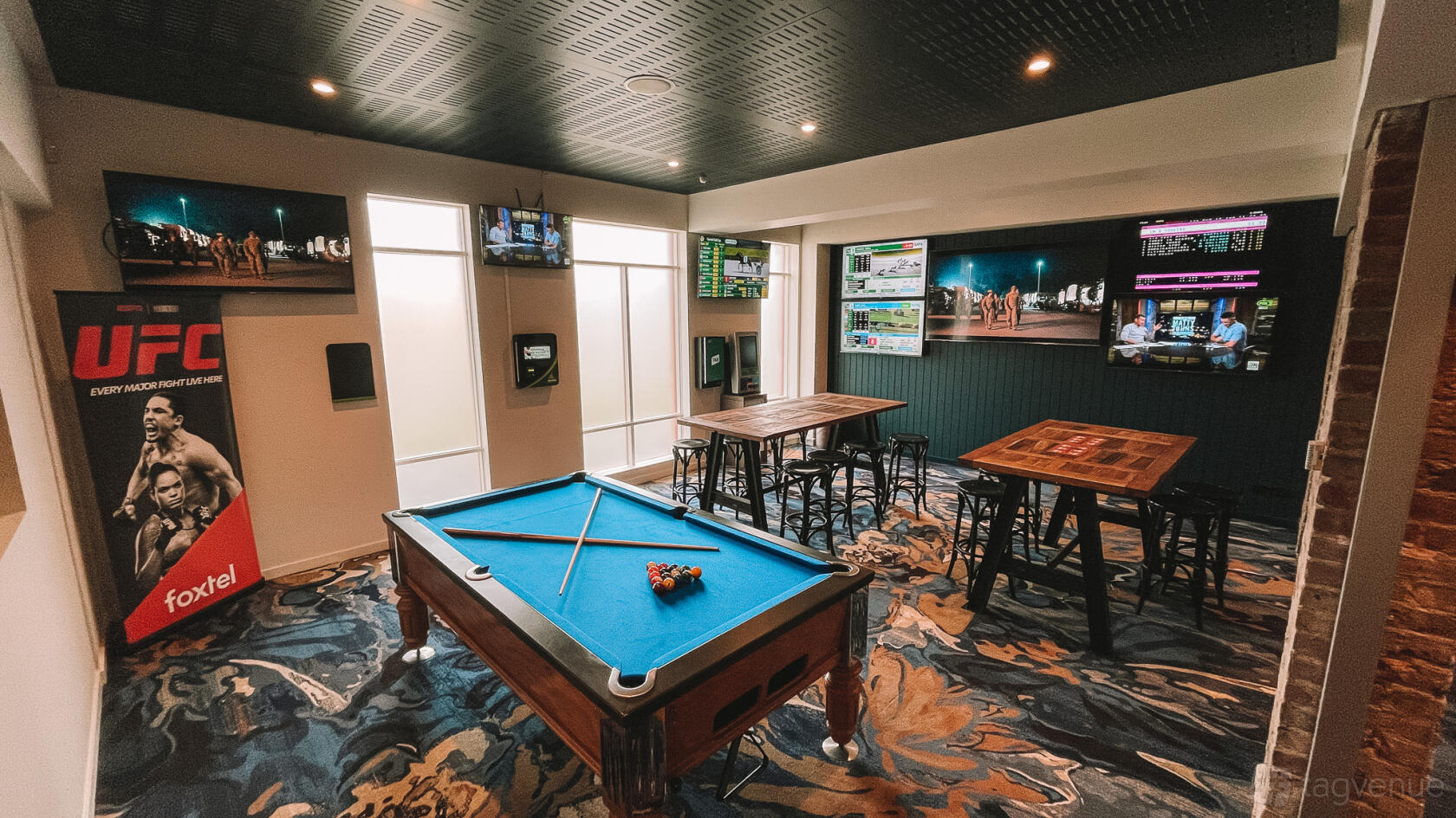 A pub with a pool table, high tables with stools, and multiple wall-mounted TVs at Grosvenor Hotel.