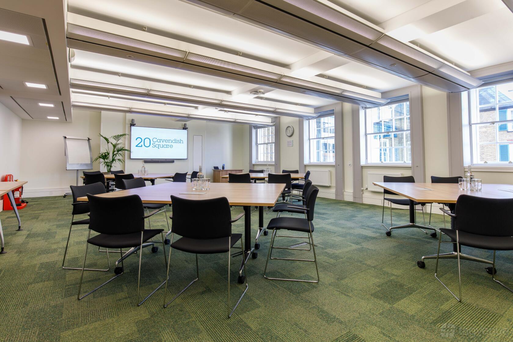 A training room with round tables, black chairs, a projector screen, and large windows at 20 Cavendish Square.