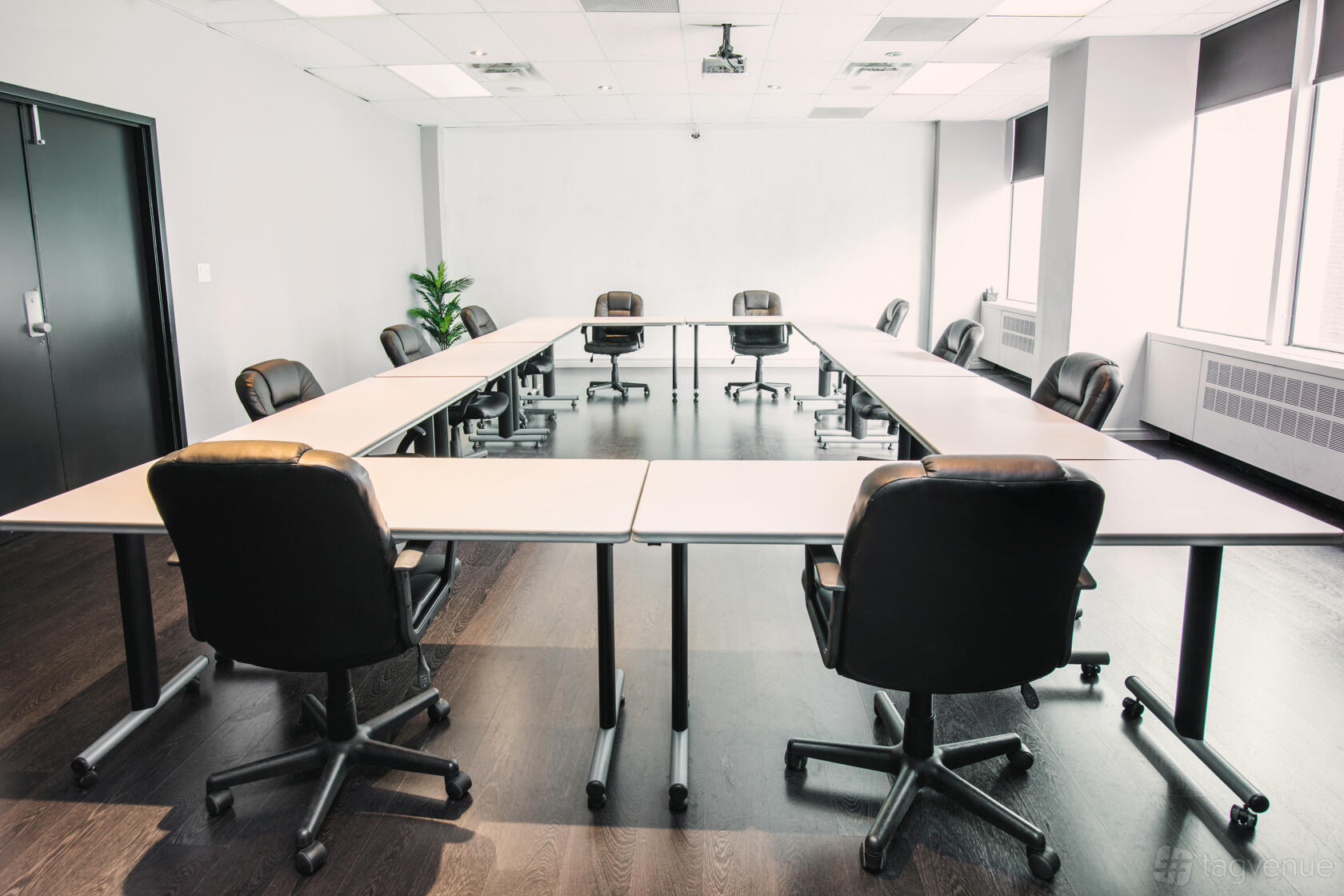 A boardroom with a U-shaped table arrangement, black rolling chairs, and a projector at The Village Hive Eglinton.