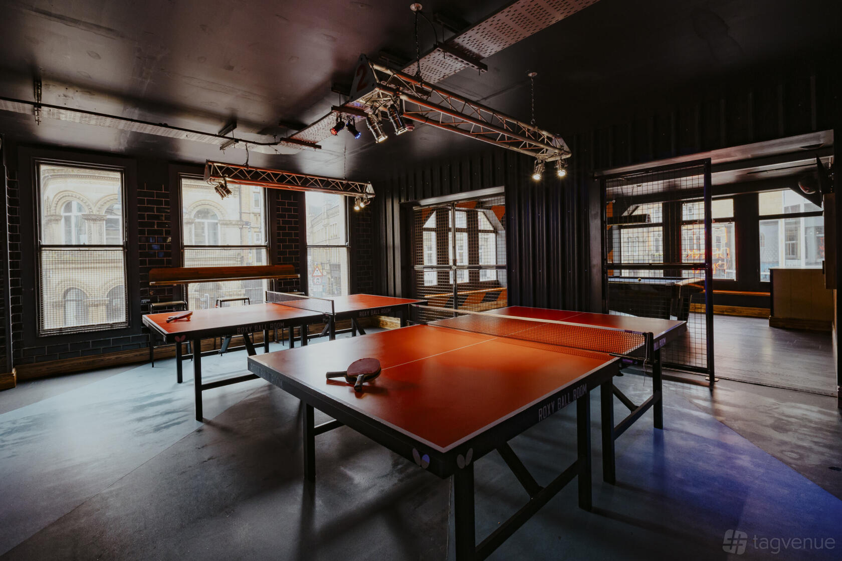 An event space in a bar with red ping pong tables, large windows, and industrial lighting at Roxy Ball Room Leeds Boar Lane.