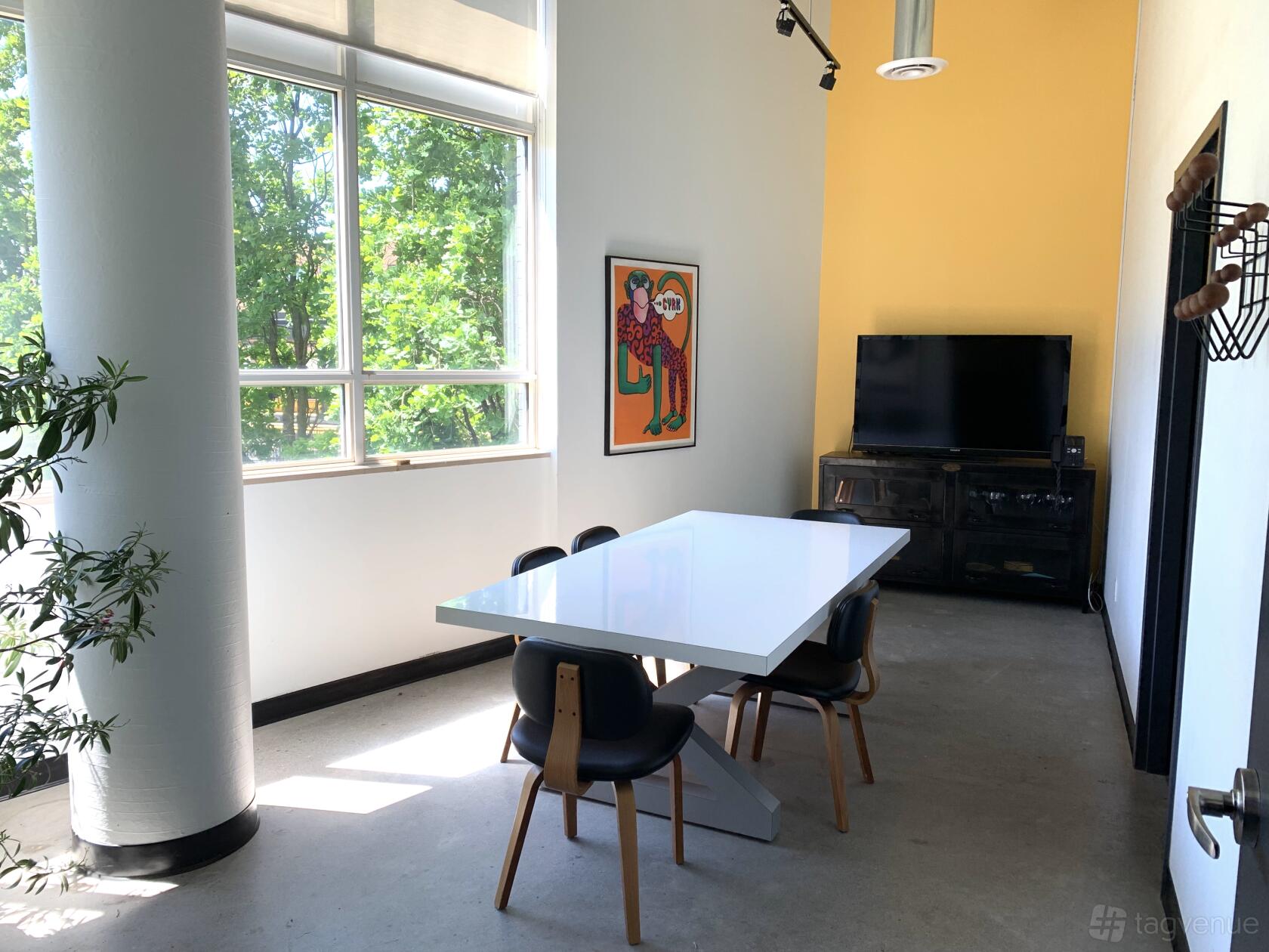 A meeting room with a white conference table, black chairs, large windows, and a flat-screen TV at Powerhouse Casting.