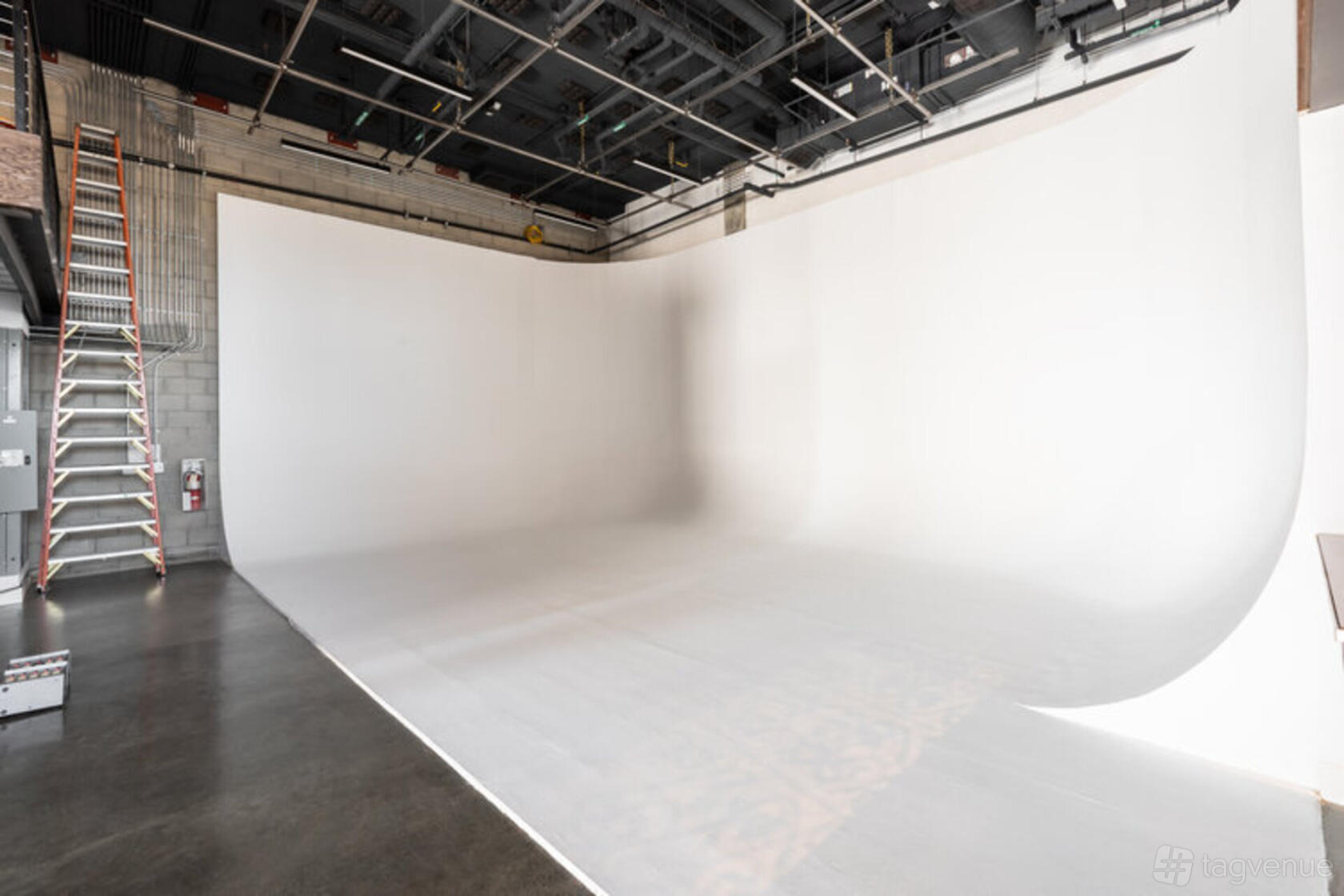 A photo studio with a large white cyclorama wall, concrete floors, and exposed ceiling at Solar Studios.
