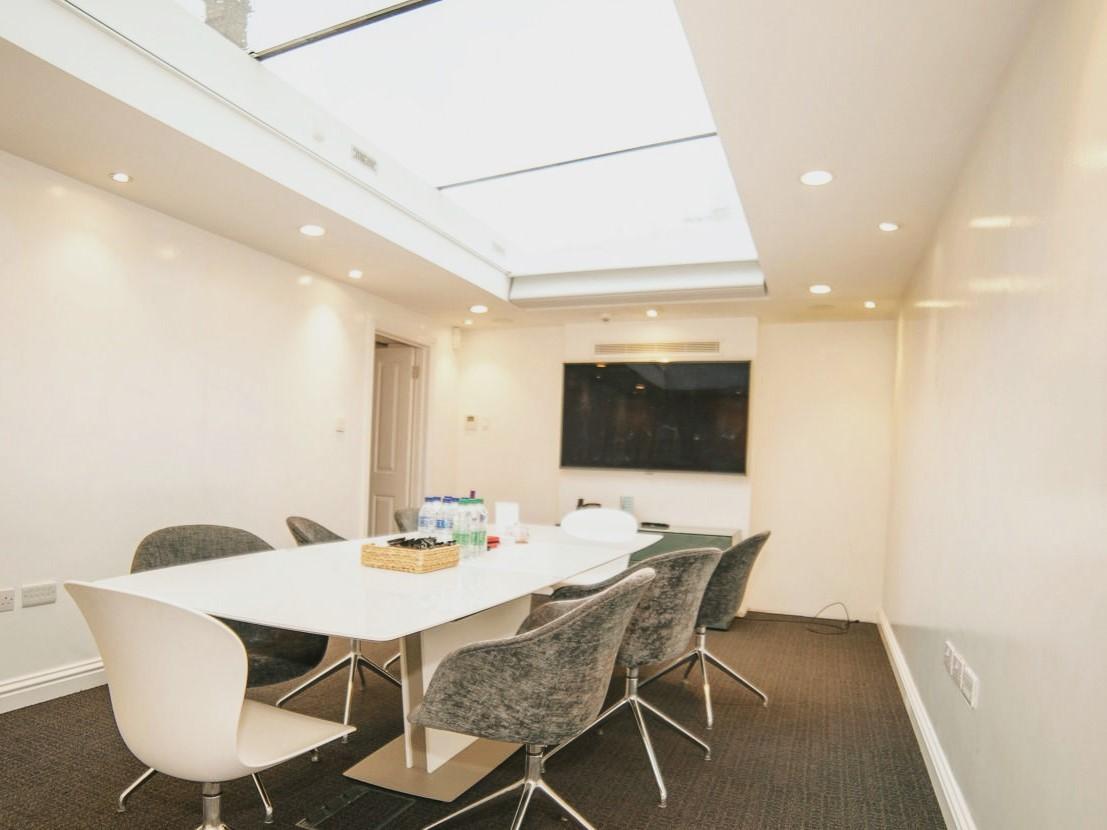 A meeting room with a skylight, a large white table, modern chairs, and a wall-mounted screen at IdeaSpace London.
