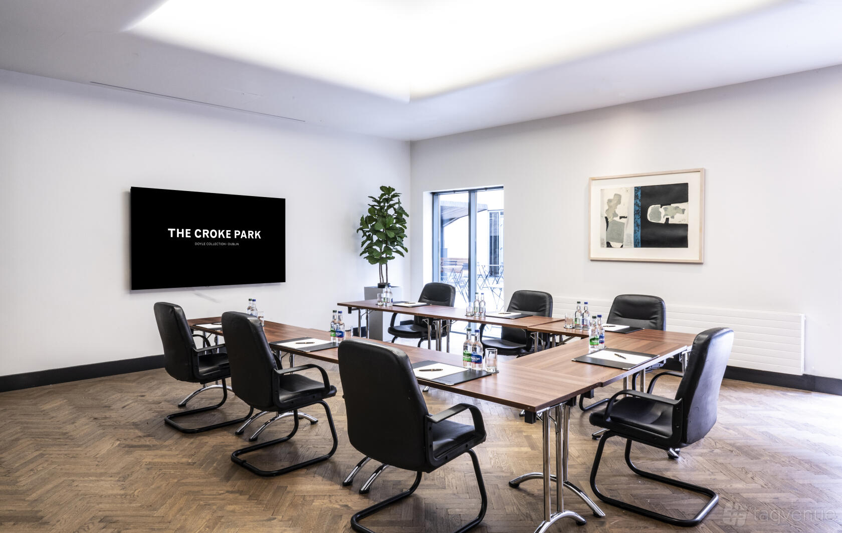 A hotel meeting room with a U-shaped wooden table setup, black leather chairs, and large display screen at The Croke Park Hotel.