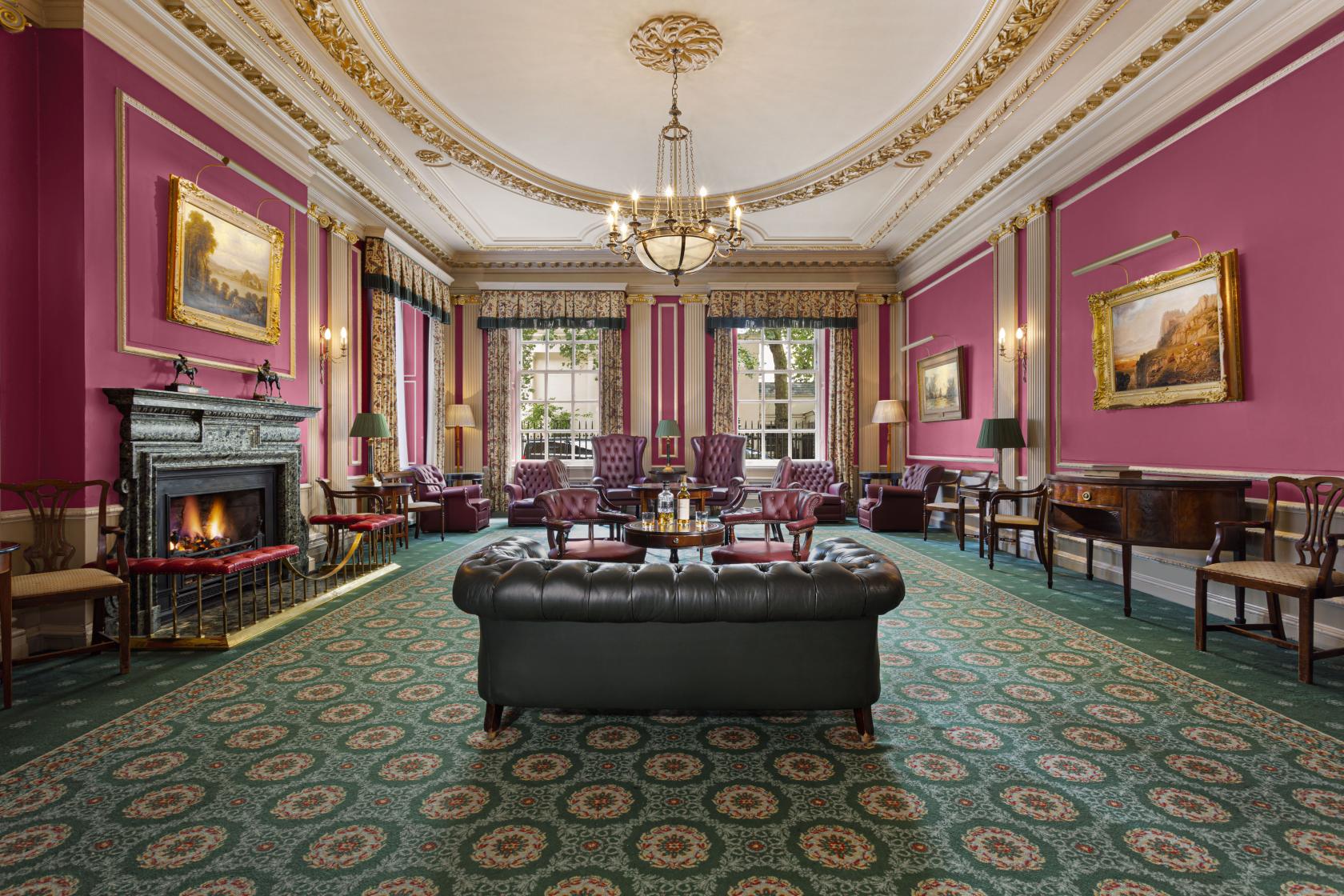A function room with ornate gold-trimmed ceiling, pink walls, a fireplace, and leather seating at The Caledonian Club.