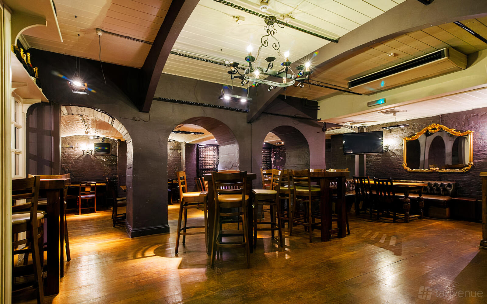 An underground bar with arched brick alcoves, wooden floors, tall tables, and vintage chandeliers at The King's Head Pub.