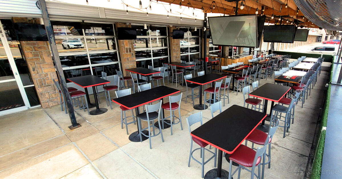 An outdoor bar area with black tables, red chairs, multiple TVs, and string lights at Texas Huddle.