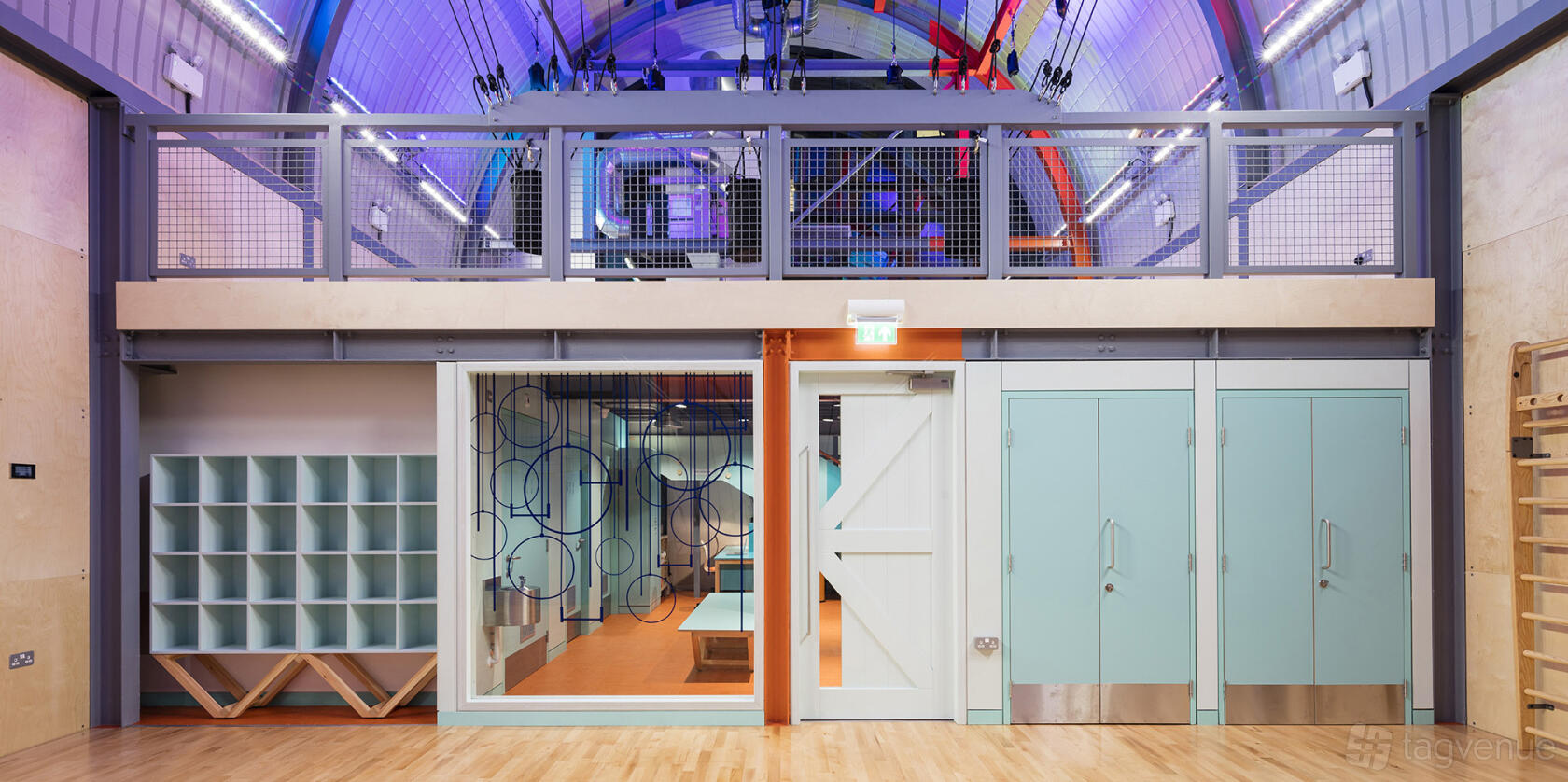 A sports hall with high ceilings, colorful lighting, wall-mounted gym rings, and glass-walled studio at Flying Fantastic Union Street.