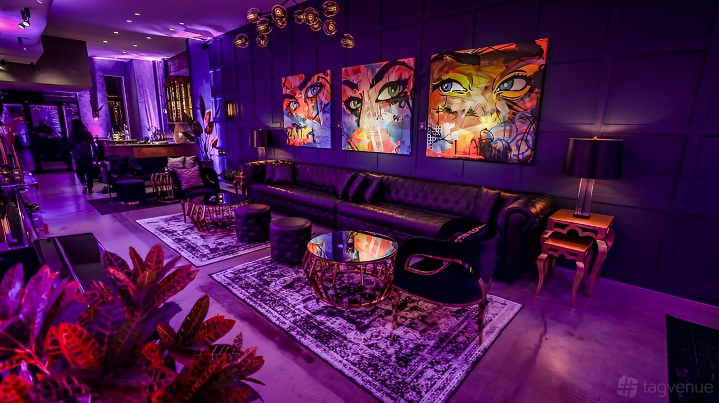 An event venue with purple accent lighting, tufted leather sofas, bold wall art, and gold-trimmed tables at TwoFortyThirty.