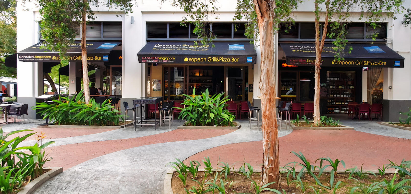 A restaurant terrace with outdoor tables, black umbrellas, and surrounding greenery at Hannibal.