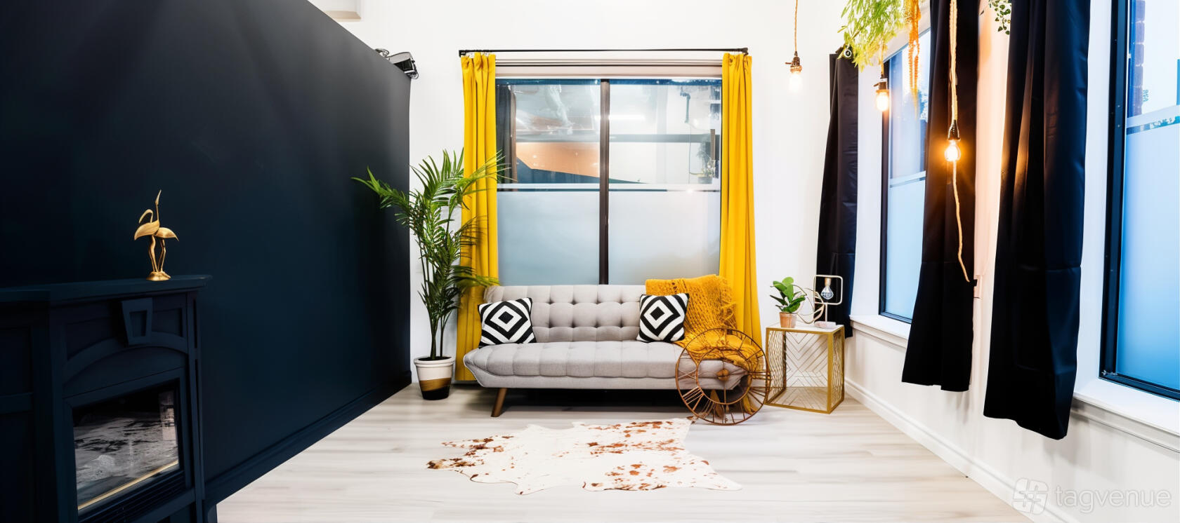 An event venue with a gray tufted sofa, yellow curtains, potted palm, and cowhide rug at Velvet Season Studios.