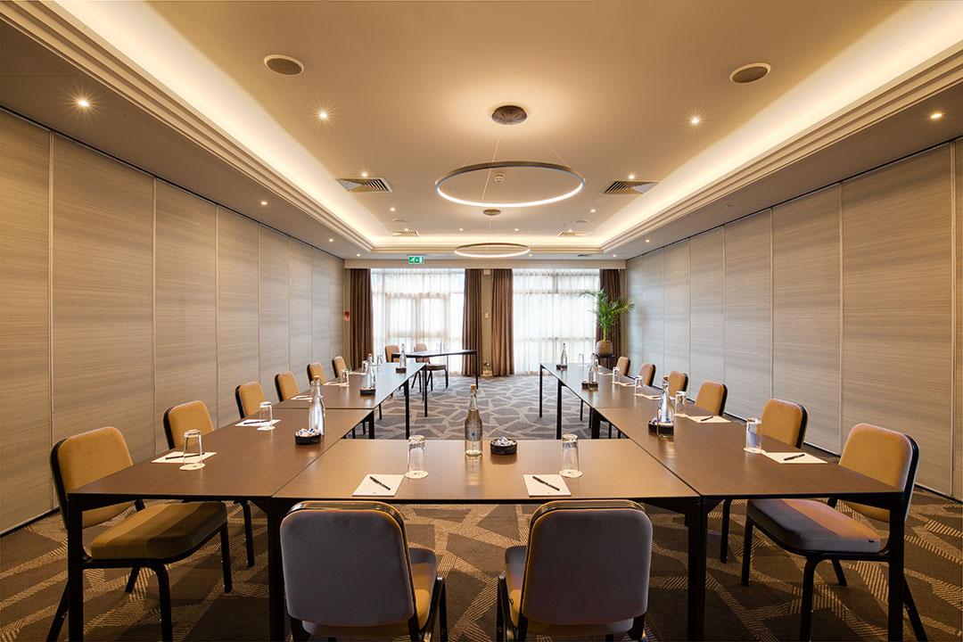 An event space with U-shaped tables, neutral walls, and large windows with sheer curtains at DoubleTree by Hilton London - Ealing.