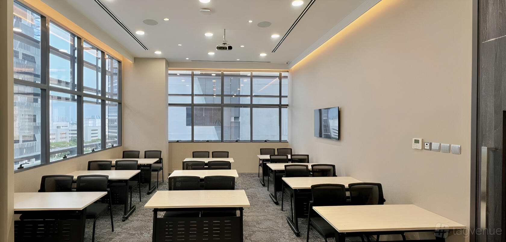 A meeting room with rows of tables and mesh chairs, large windows, a wall-mounted screen, and ceiling projector at Fine Wines SG.