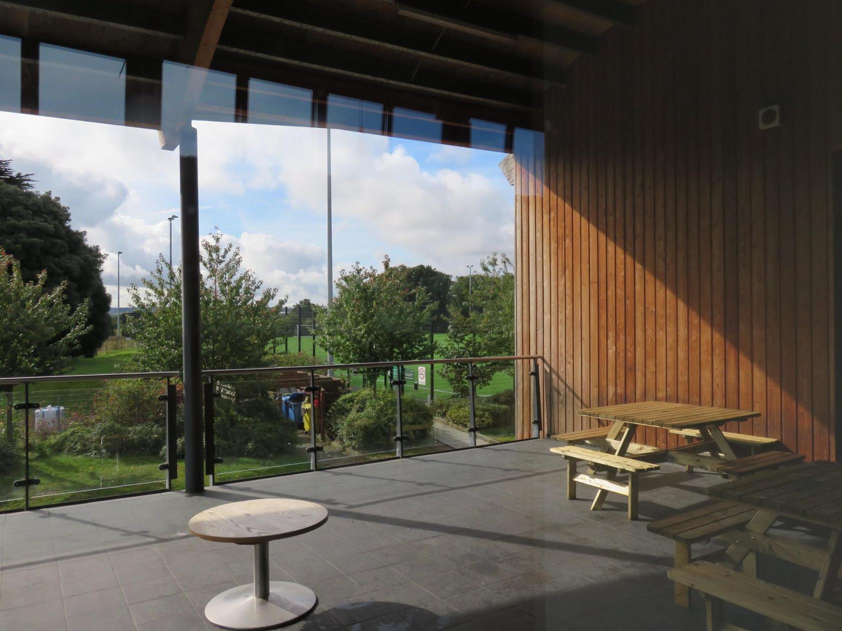 An outdoor terrace with wooden picnic tables, glass railing, and park views adjoining the Park Suite at Princes Park.