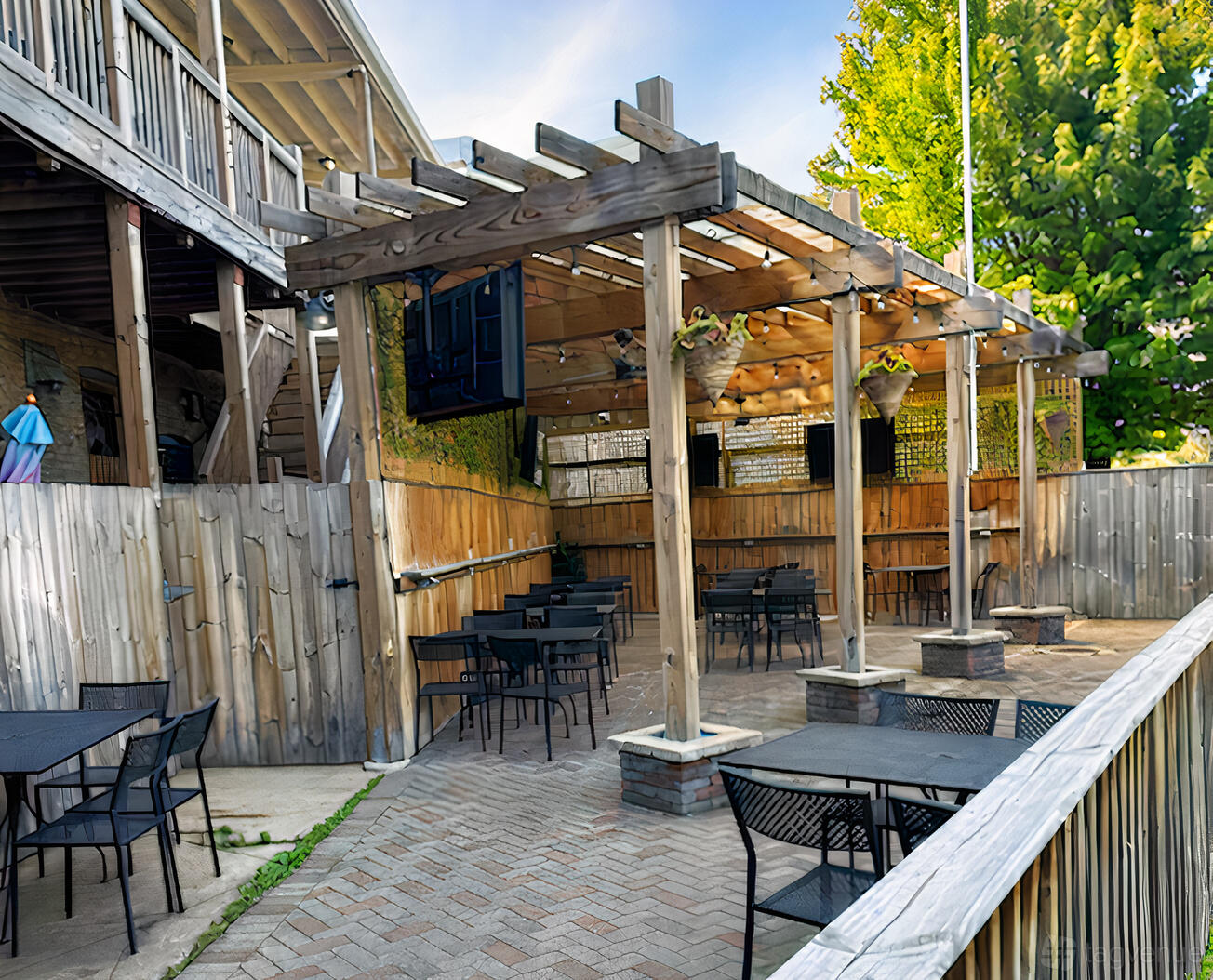 An outdoor bar space with a wooden pergola, hanging planters, and black metal tables at Almost Home Tavern & Grill.