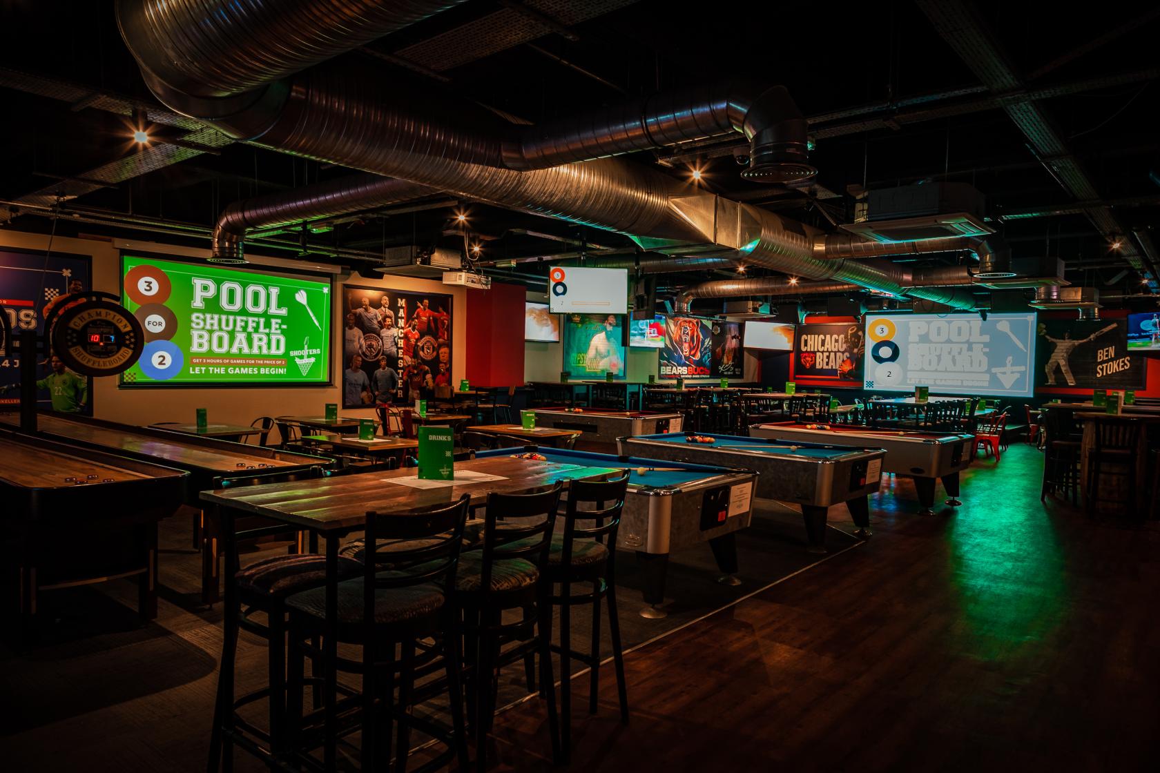 A brewery sports bar with pool tables, shuffleboard, large sports screens, and exposed ductwork at The Bierkeller Manchester.