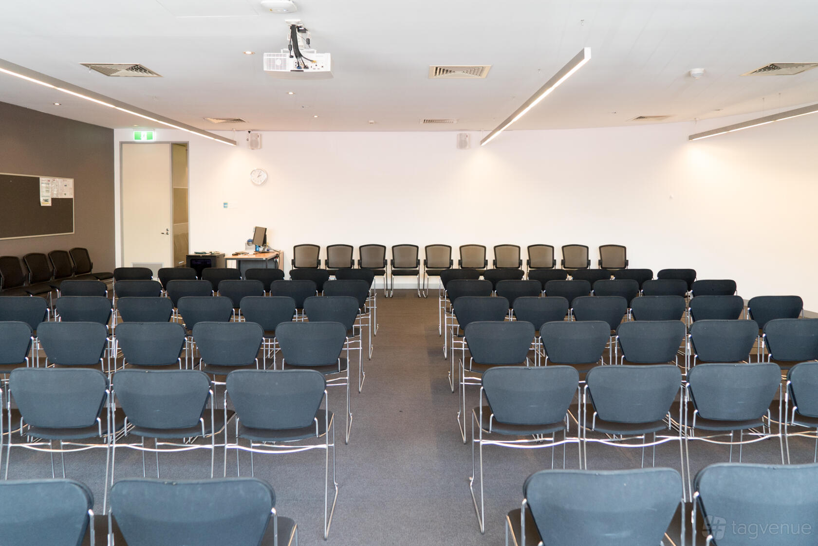 A meeting room with rows of black chairs facing a white wall and two ceiling projectors at Melbourne Business School.