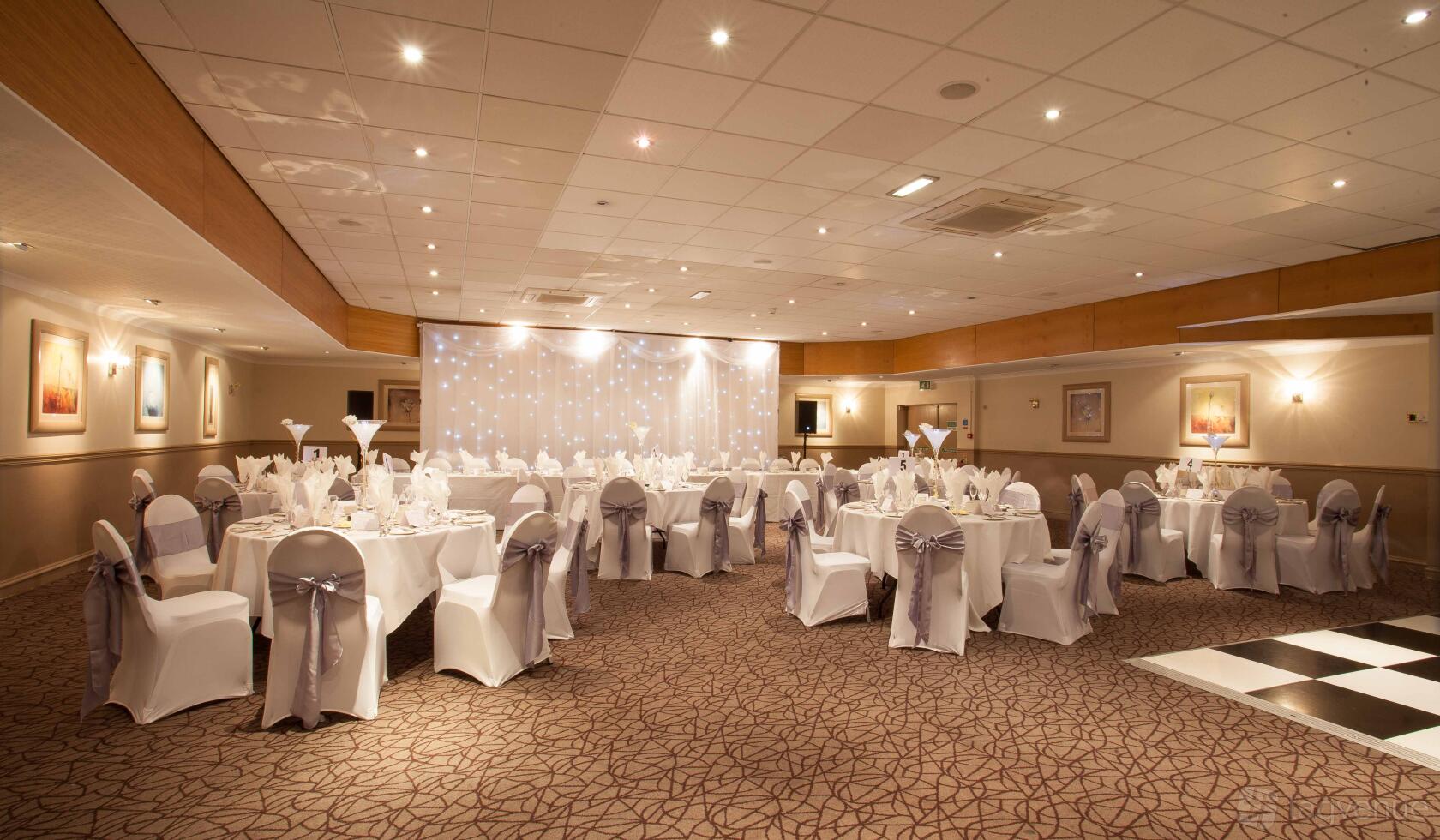 A meeting room with round tables dressed in white linens and chair covers with bows at Cresta Court Hotel.