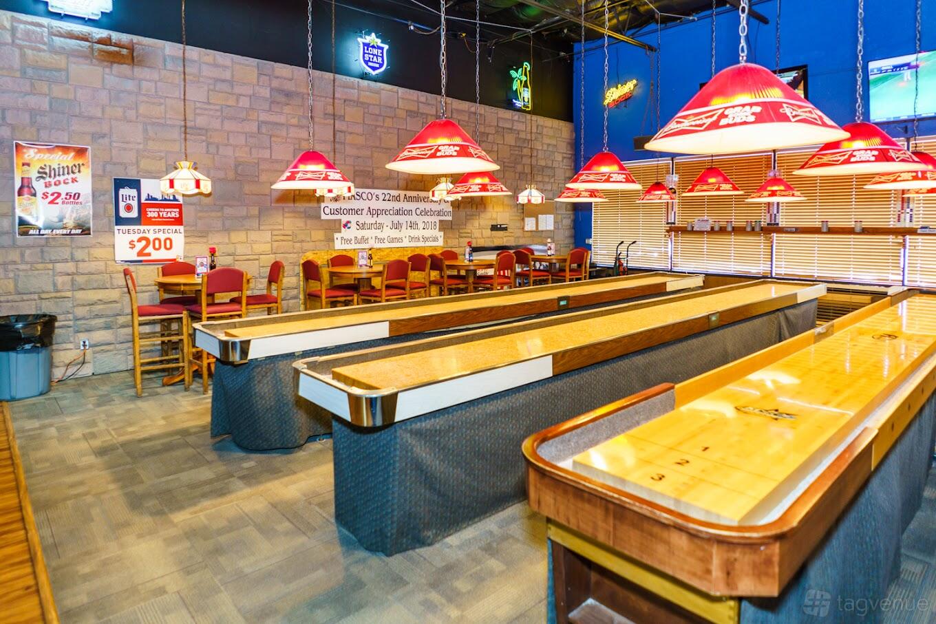 An event space in a bar with shuffleboard tables, stone accent walls, and red pendant lights at Fiasco Cocktails & Sports Bar.