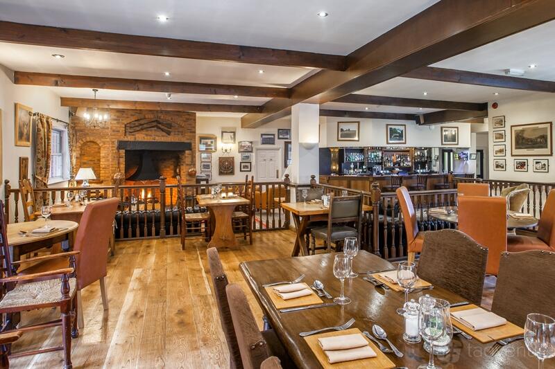A restaurant with wooden floors, exposed beams, a brick fireplace, and framed art on the walls at Fox & Hounds.