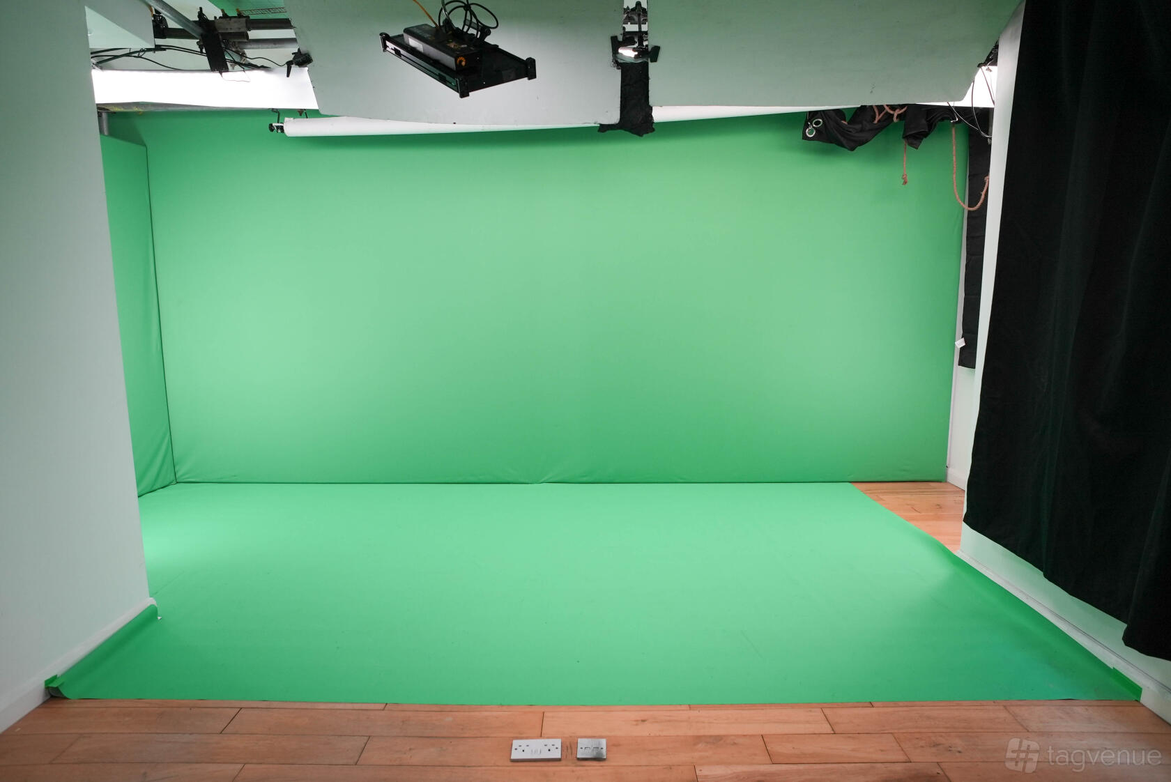 A photo studio with a large green screen backdrop, wooden floors, and ceiling lighting at 90° Green Screen/Colourama Studio.