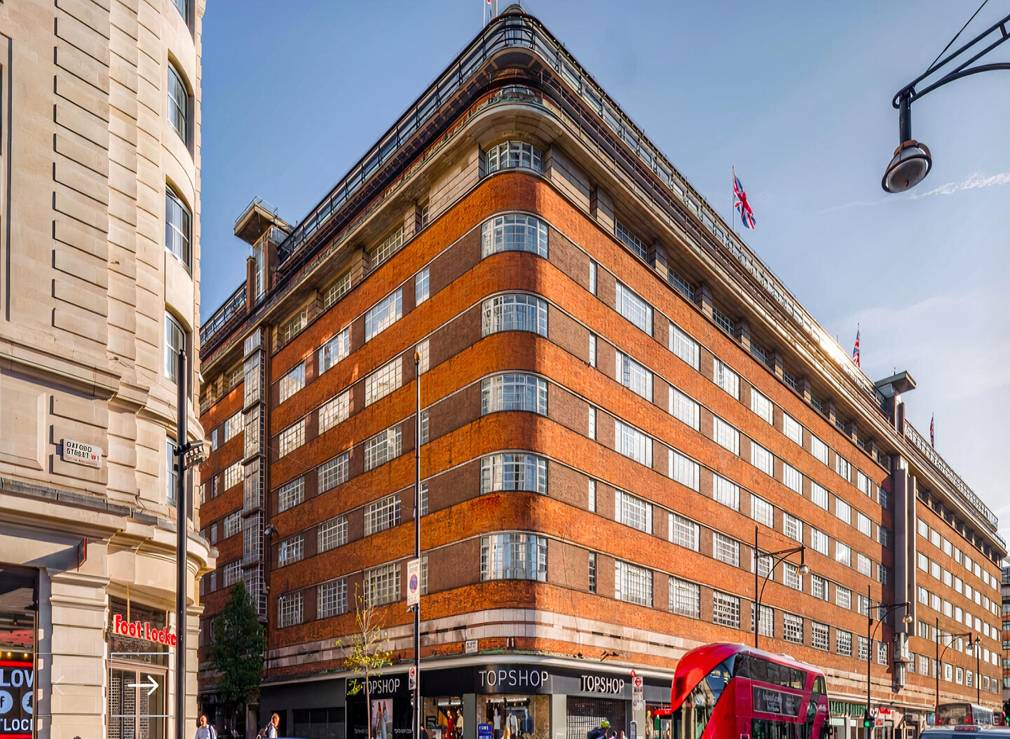 A large brick hotel with curved corners, horizontal window bands, and British flags at The Marble Arch Hotel.