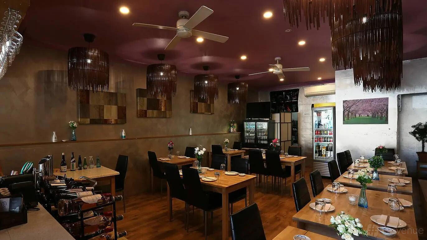An event space in a restaurant with wooden tables, black chairs, decorative pendant lights, and wall art at RK San.