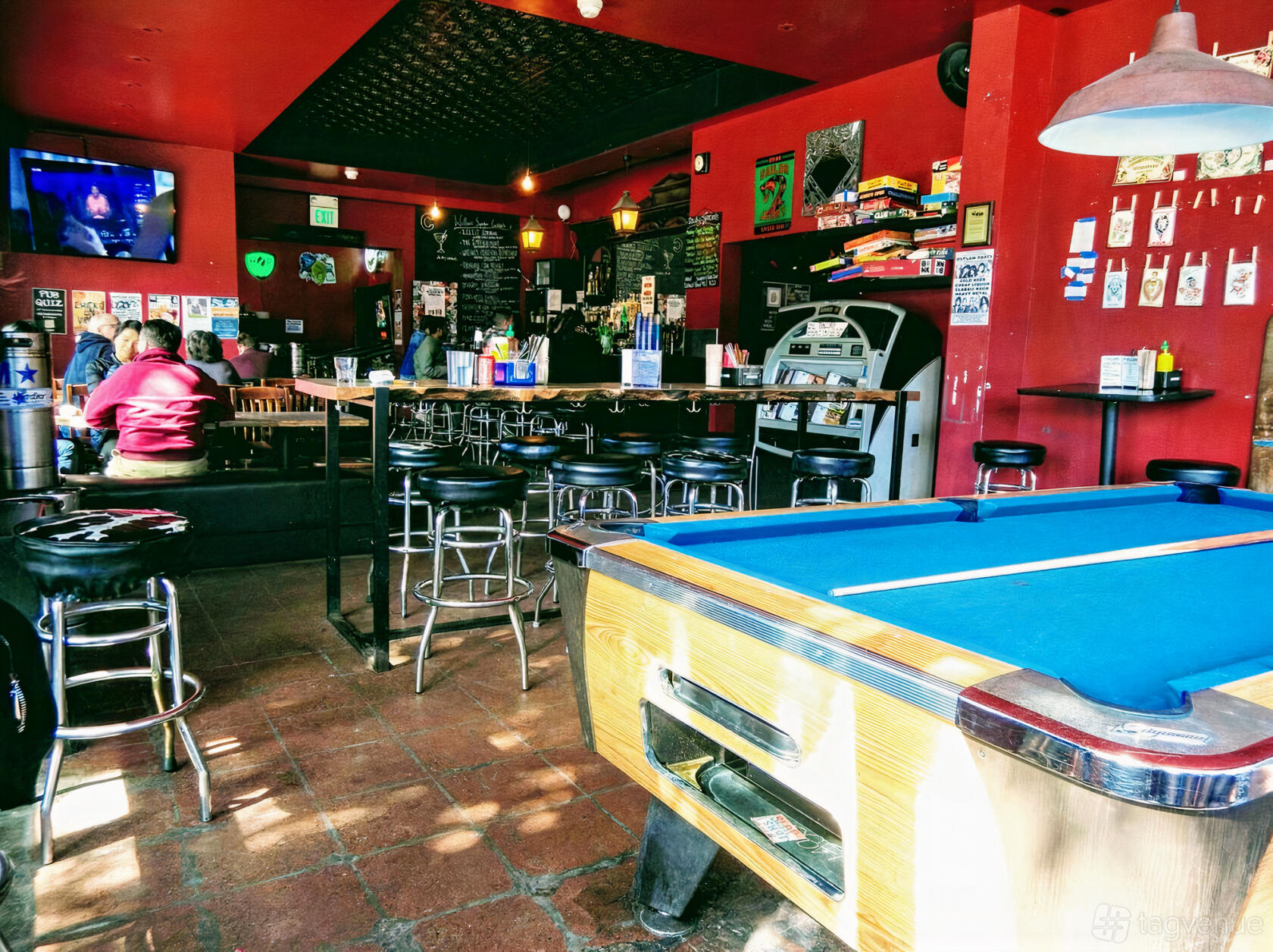 A bar with a blue pool table, high-top tables, red walls, and a jukebox at The Willows.