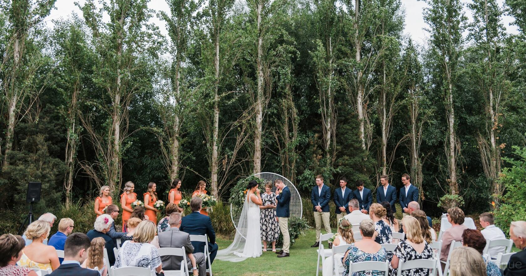 An outdoor event venue with a grass lawn, tall trees, and white folding chairs at Tailrace Centre.