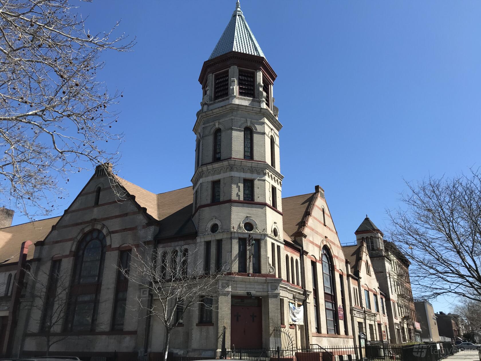 A historic warehouse with tall arched windows, stone façade, and a prominent clock tower at Gymnopedie.