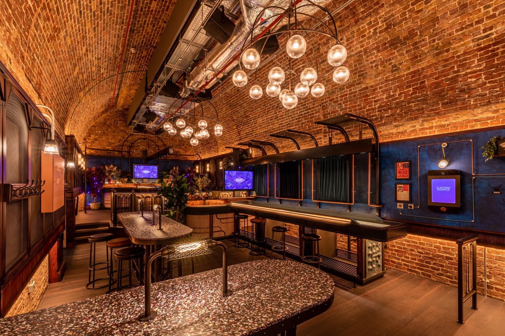 An event space in a cocktail bar with arched exposed brick ceiling, globe pendant lighting, and terrazzo tables at Electric Shuffle London Bridge.