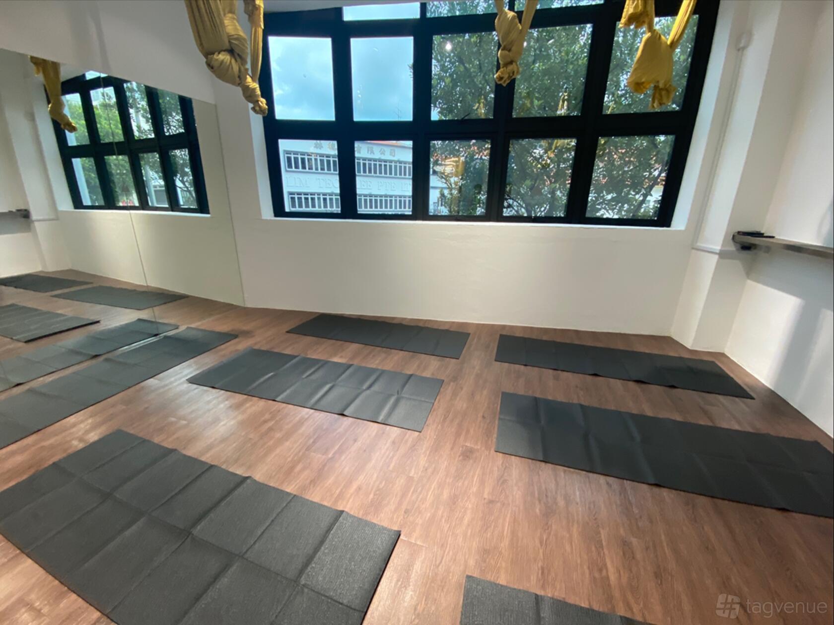 A dance studio with floor-to-ceiling windows, wooden floors, and black yoga mats at Ministry of Yoga Wellness.