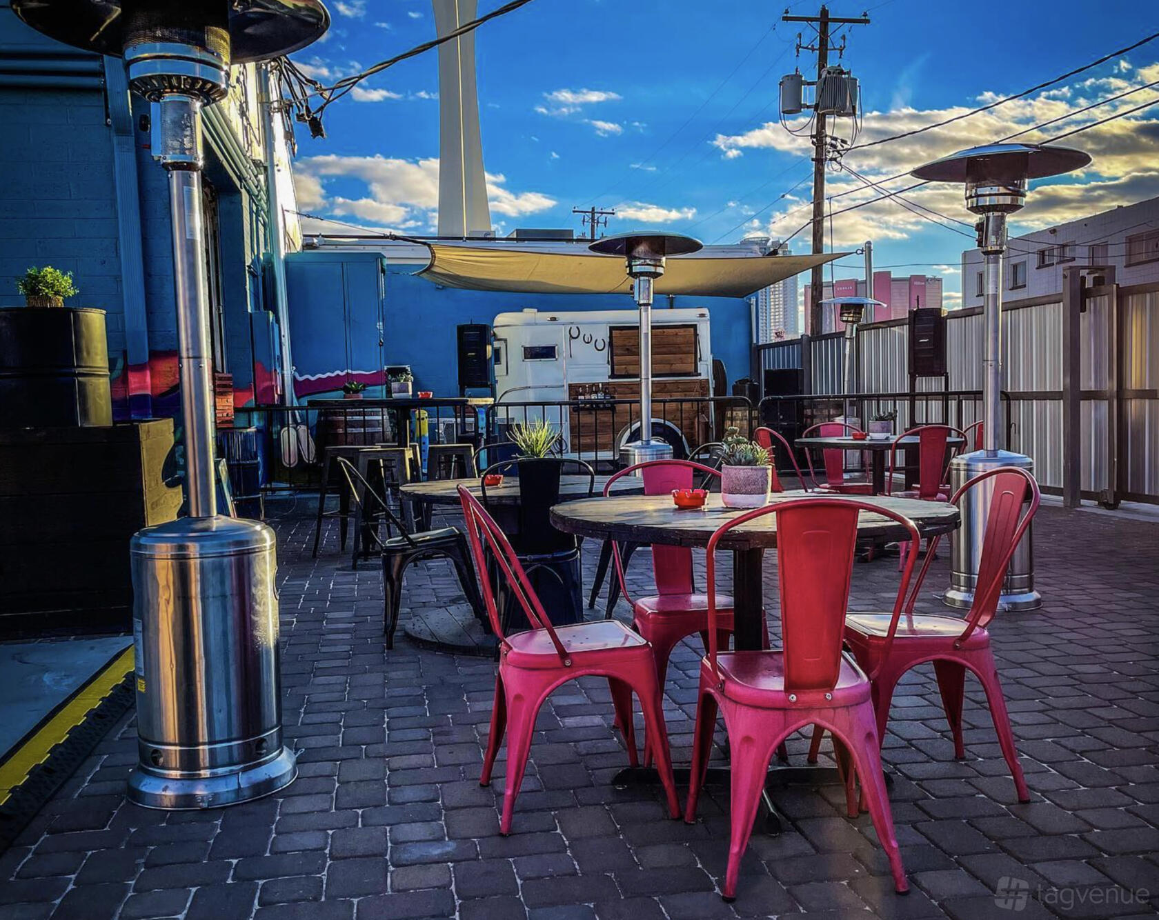 An outdoor event space with metal chairs, round tables, patio heaters, and string lights at Horse Trailer Hideout.