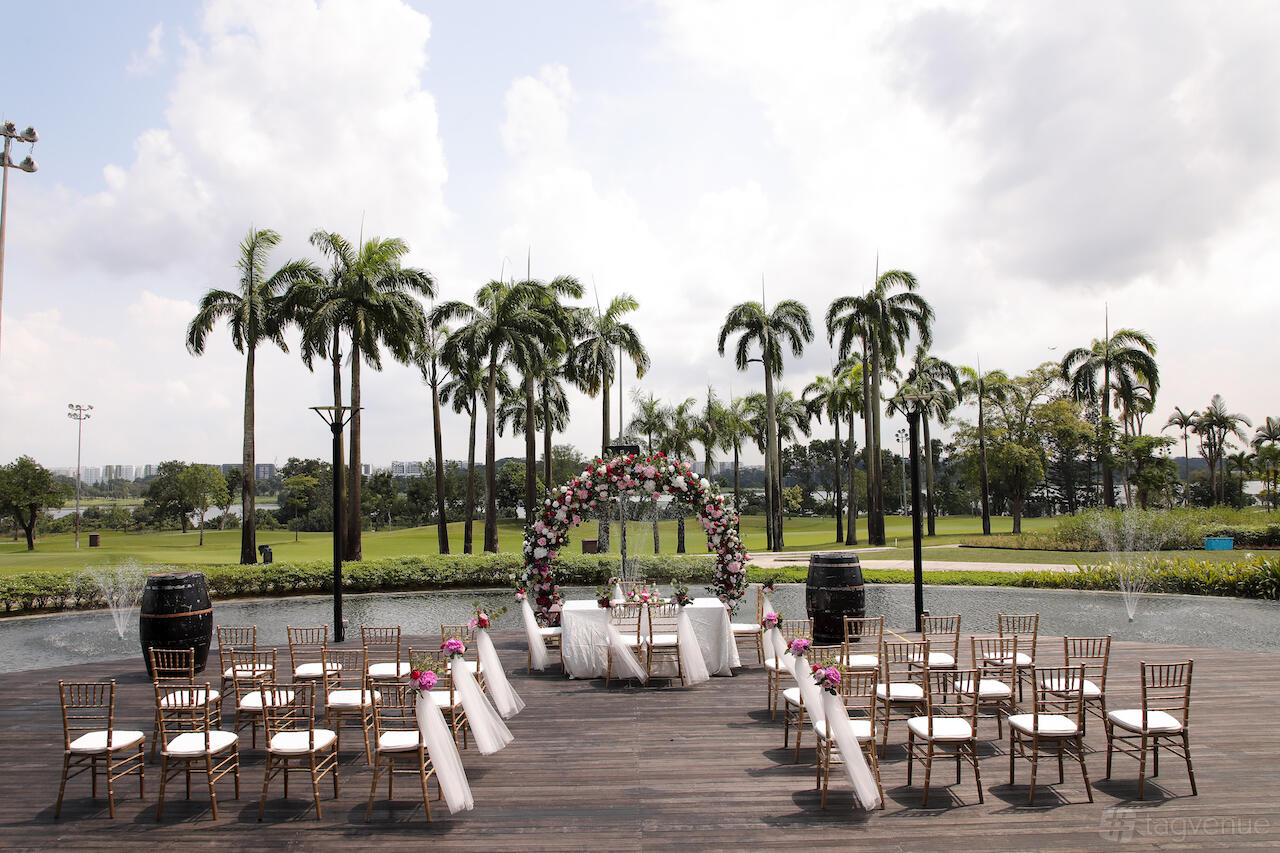 An outdoor terrace with a floral wedding arch, white chairs, and palm trees at Seletar Country Club.