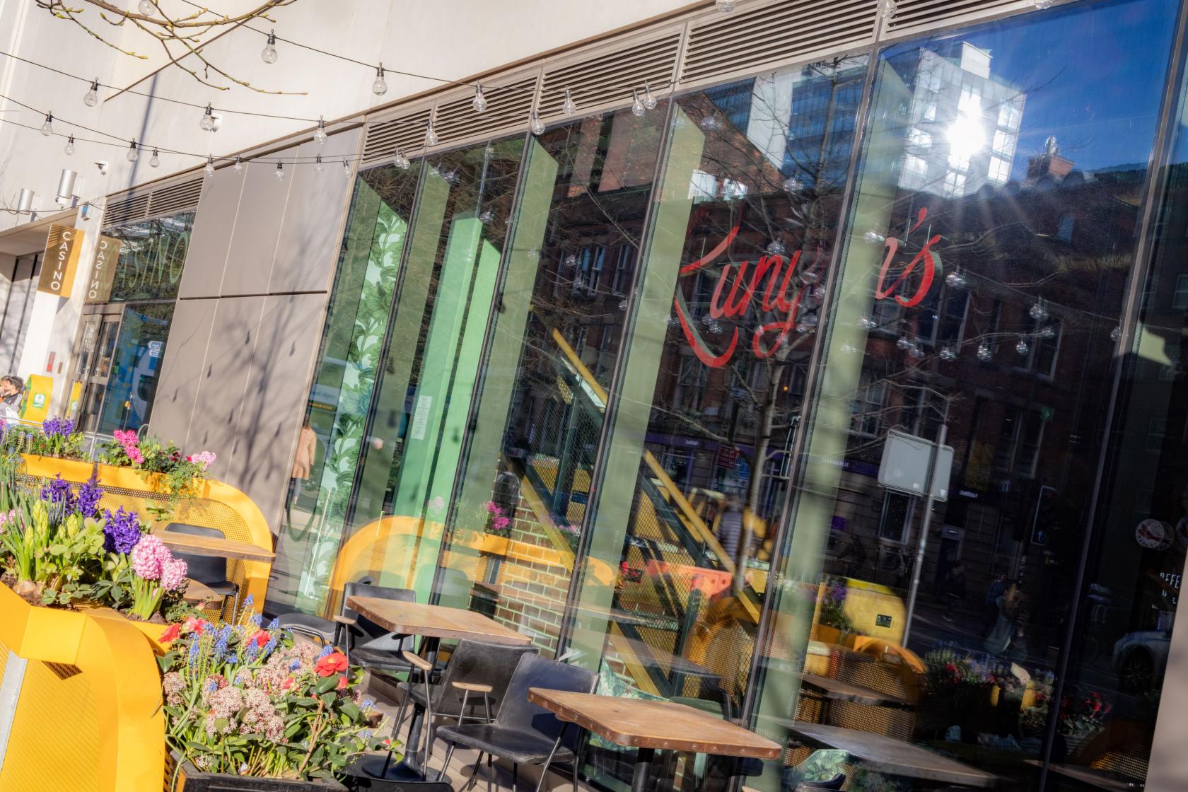 An outdoor event space with wooden tables, yellow benches, and colorful flower planters at voco Manchester.