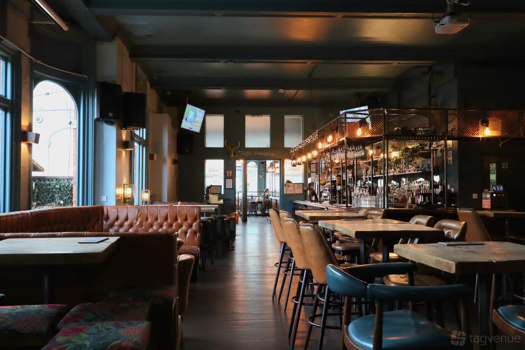 A bar with tufted leather banquettes, high tables with stools, and hanging pendant lights at The Regent Balham.