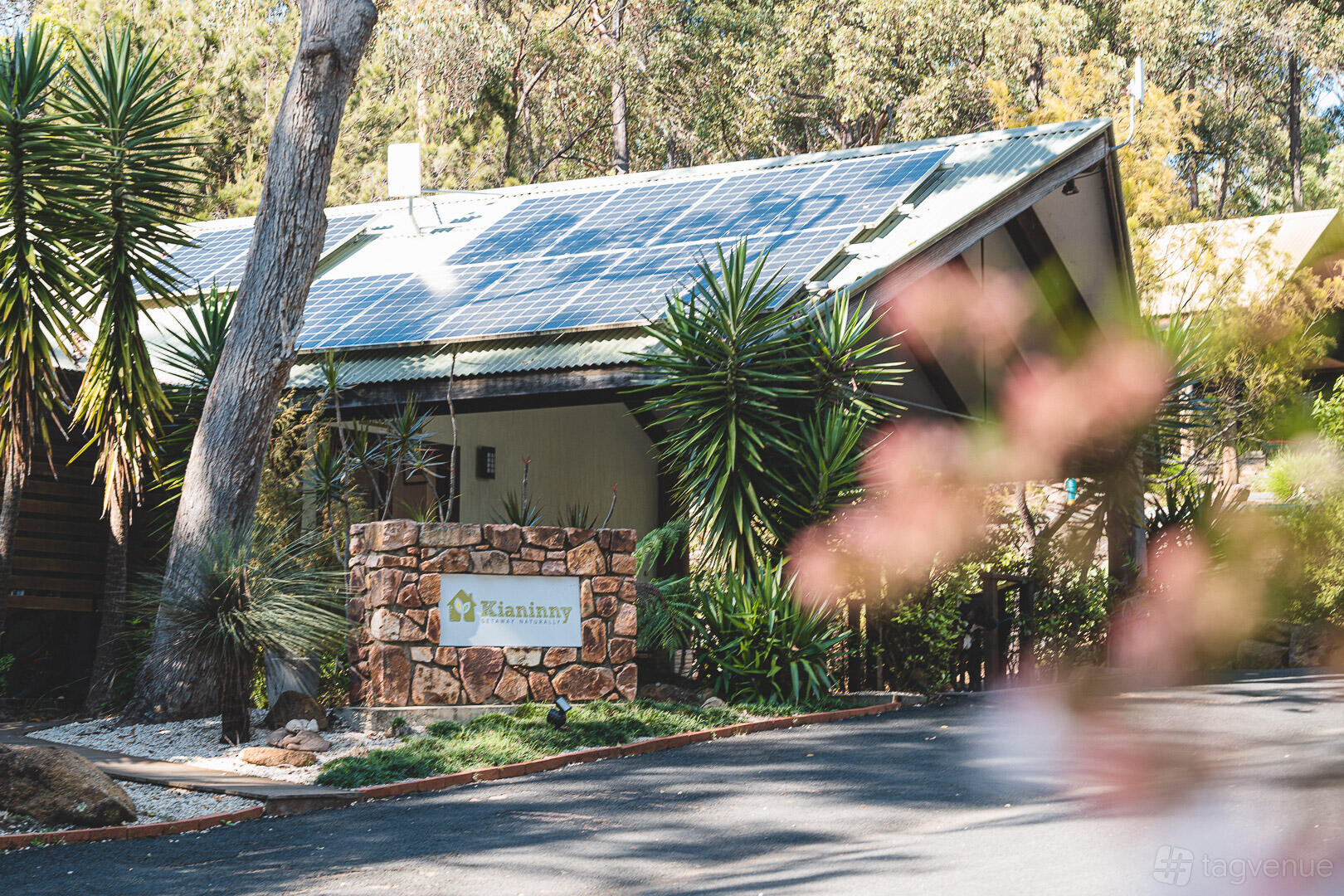 An outdoor venue with a stone entrance sign, native plants, and a solar-paneled roof at Kianinny.