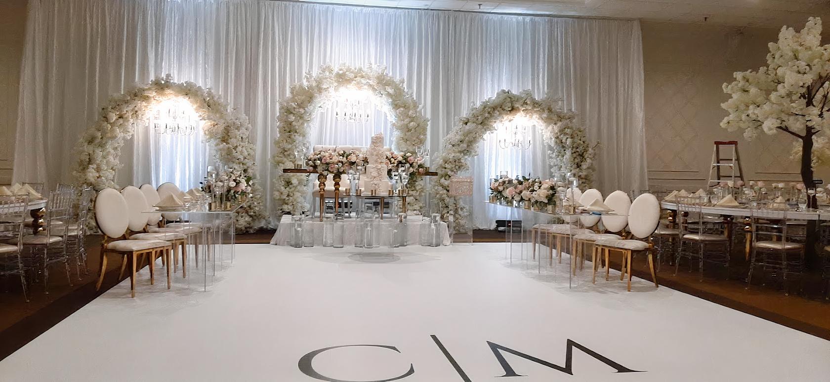 A hall with floral archways, chandeliers, and a white stage floor at Edessa Banquet Hall and Convention Centre.