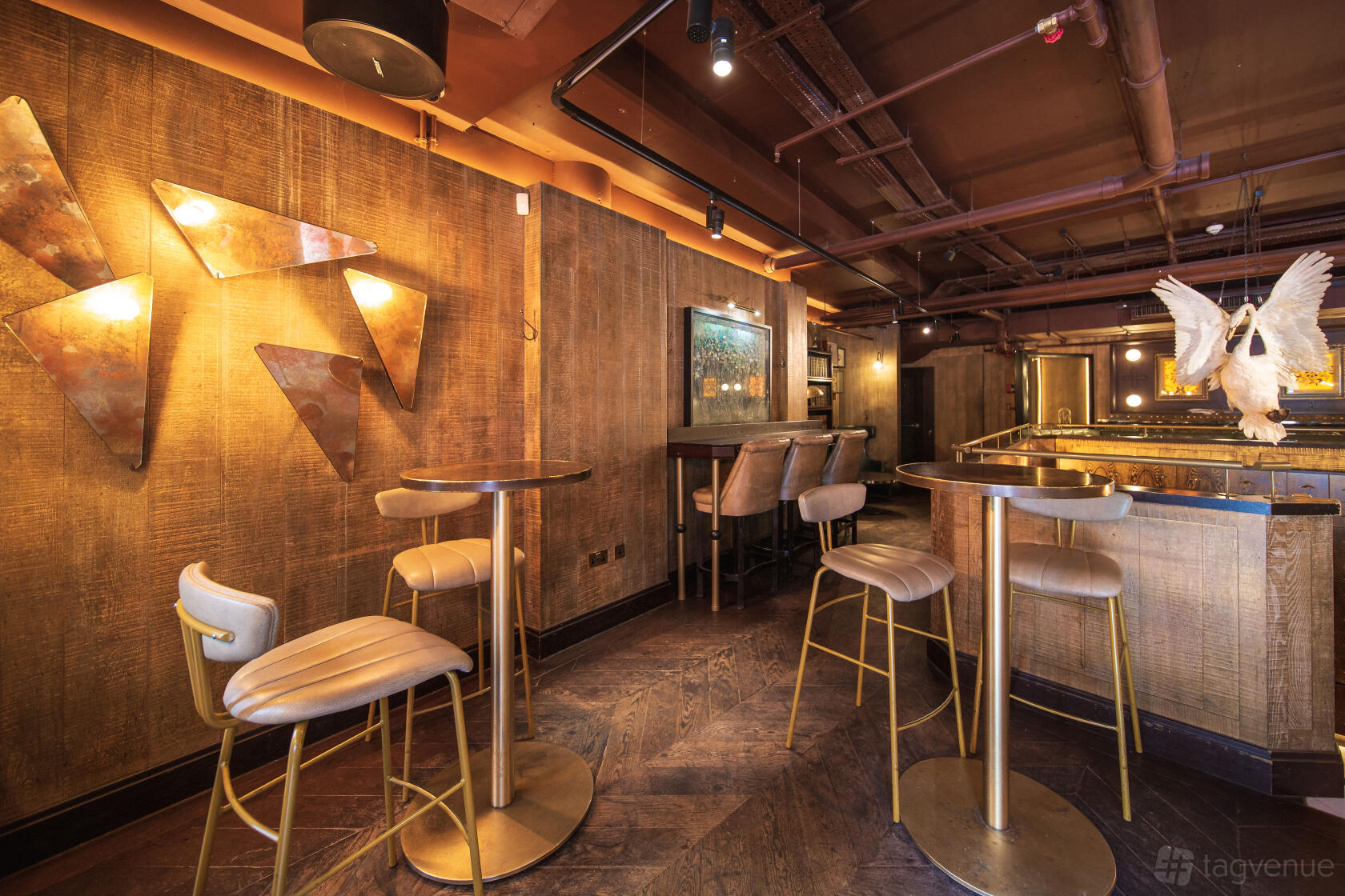 A cocktail bar with gold accents, high tables and chairs, textured walls, and sculptural lighting at The Botanist Broadgate Circle.